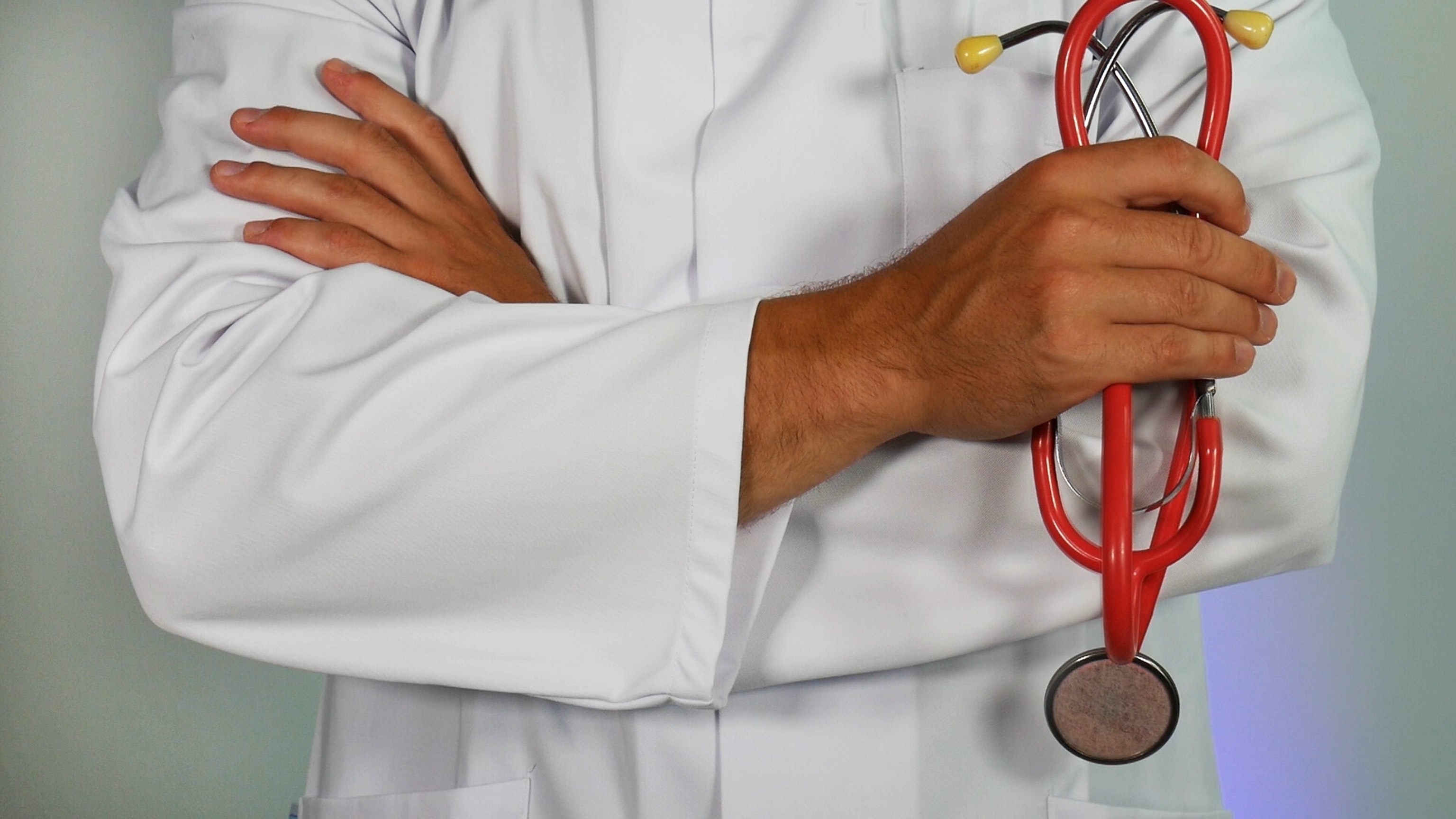 Imagen de doctor cruzado de brazos sosteniendo un estetoscopio rojo