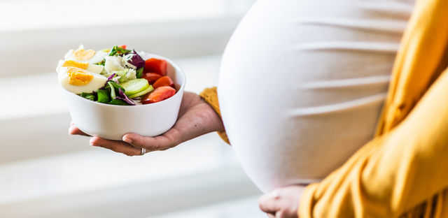 Imagen de mujer embarazada sosteniendo un plato de ensalada.