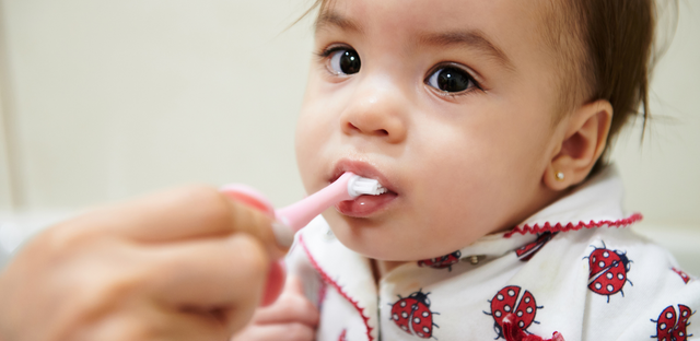 Imagen niña donde un adulto le cepilla sus dientes.